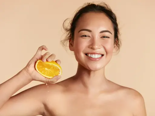 Donna sorridente con fetta d'arancia, suggerisce che il siero alla vitamina C si può usare in estate per una pelle luminosa.