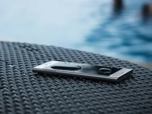 Smartfon z kroplami wody na ekranie, leżący na plecionej powierzchni. Dowód, że ip67 co oznacza: odporność na zanurzenie.