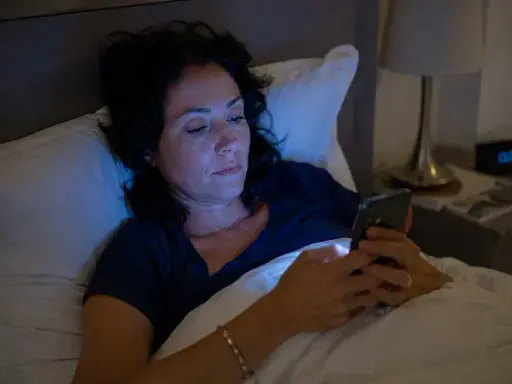 Une femme dans son lit, éclairée par la lumière bleue de son téléphone, perturbant son sommeil.