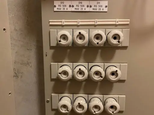 Säkringsskåp med keramikproppar, alla märkta MAX 20 A. En diskussion om prisskillnad mellan 16 A och 20 A säkringar kan uppstå.