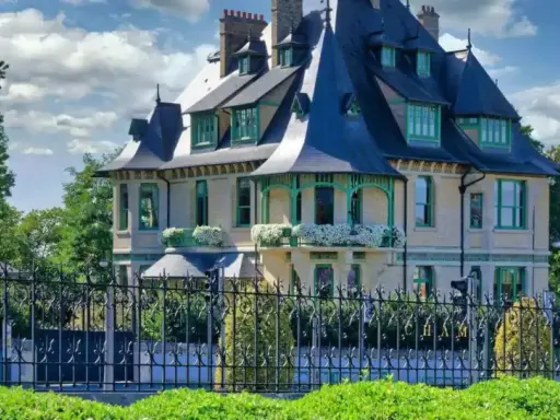 La villa Demoiselle à Reims, une demeure d'exception avec ses toits bleus et ses ornements verts, se dresse fièrement derrière une grille ouvragée.