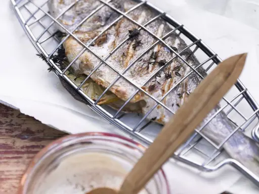Ein ganzer Fisch liegt in einem Grillkorb, bereit zum Fisch grillen. Zitronenscheiben und Kräuter sind darin versteckt.