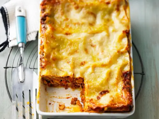 Eine frisch gebackene Lasagne al forno mit goldbraun überbackener Käseschicht, daneben ein Servierheber.