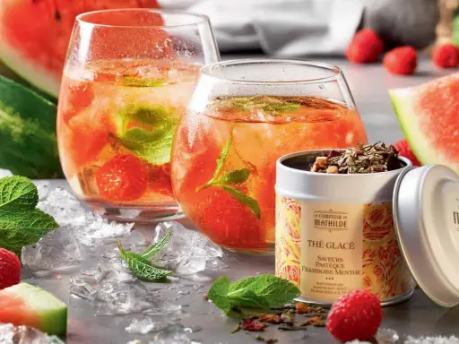 Rafraîchissante recette thé glacé : deux verres remplis de glaçons, fruits rouges et menthe, accompagnés de pastèque et d'une boîte de thé.