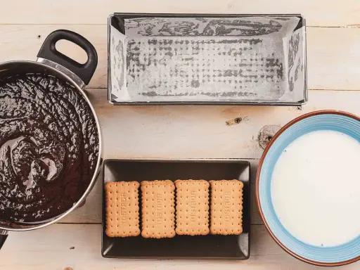 Preparando una deliciosa tarta de galletas y chocolate: chocolate derretido, galletas, molde y leche listos para mezclar.