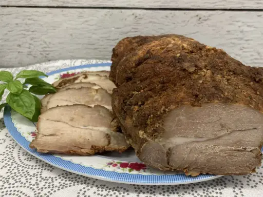 Soczysta łopatka pieczona w rękawie, pokrojona w plastry, z gałązką bazylii na talerzu.