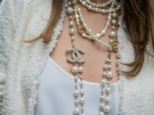 Eleganckie stylizacje z perłami, w tym wielowarstwowy naszyjnik Chanel z logo marki i perłami, dodają blasku białej bluzce i żakietowi.