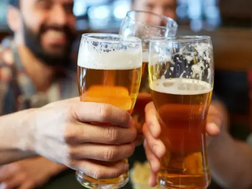 Trzech przyjaciół wznosi toast. Każdy trzyma w dłoni szklankę złocistego piwa z pianką.