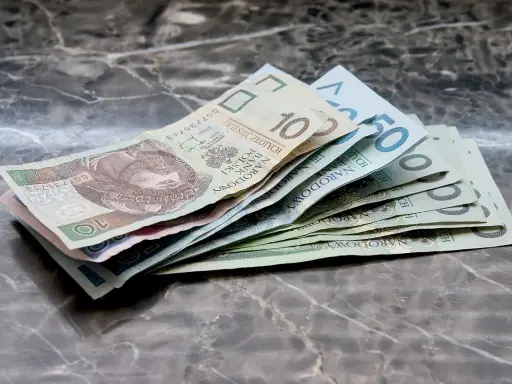Zbiór polskich banknotów, od 10 do 50 zł, leżących na marmurowym blacie. Warto wiedzieć, jak odzyskać zaległe alimenty, gdy pieniądze są tak potrzebne.