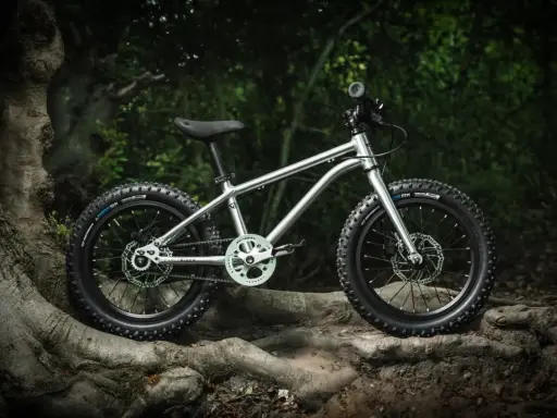 Srebrny rower dziecięcy z grubymi oponami, gotowy na wyzwania pumptracku. Jego lekka rama i solidne hamulce zapewnią bezpieczeństwo podczas pierwszych zjazdów.