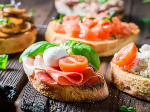 Verschiedene herzhafte Snacks auf geröstetem Brot: Bruschetta mit Tomaten, Pilzen, Schinken und Mozzarella.