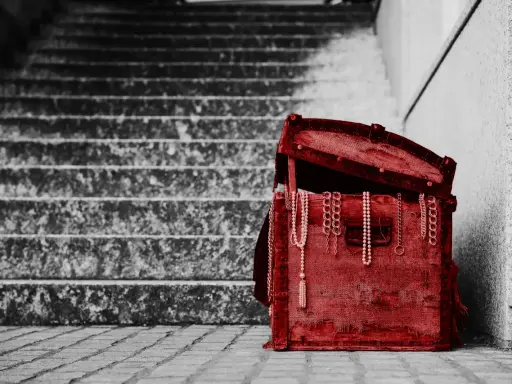 Czerwona skrzynia z biżuterią, stojąca na schodach. To pamiątka, spadek po rodzicach, pełen wspomnień.