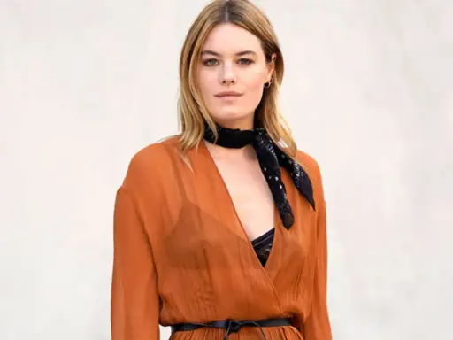 Camille Rowe luce un pañuelo negro y un vestido naranja con escote pronunciado.