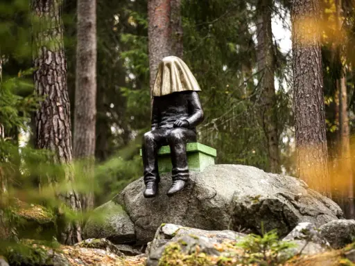 En mystisk staty med gyllene tyg över huvudet sitter på en sten i **stadsparken Falun**.