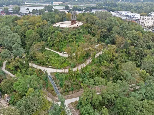 Wzgórze z pomnikiem Kotwicy, otoczone zielenią. Kręte ścieżki i schody prowadzą przez park akcji "Burza", oferując widok na miasto i Wisłę.