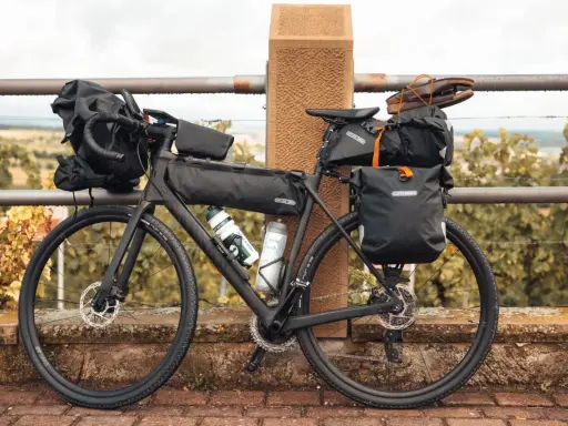 Bereit für die nächste gravel tour: Ein voll beladenes Gravelbike mit Ortlieb-Taschen, Trinkflaschen und sogar Schuhen auf dem Gepäckträger.