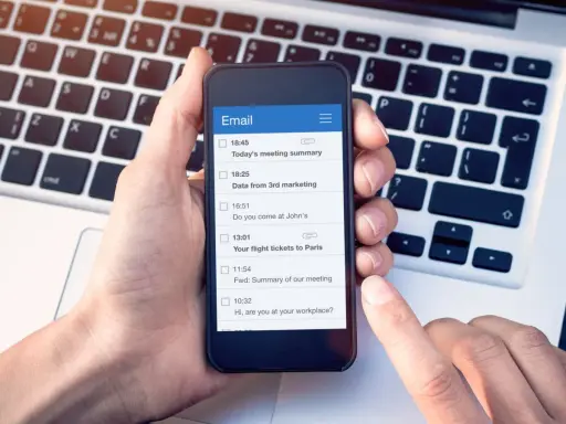 Dłoń trzyma smartfon z listą e-maili, w tym "Your flight tickets to Paris". Kiedyś, yours sincerely, wysłałbym takie wiadomości.