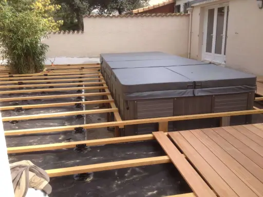Construction d'une terrasse en bois autour d'un spa. L'espacement des plots sur le plot béton est visible, prêt pour les lames de bois.