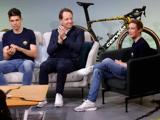 Drei Männer, darunter ein Fahrer von Jumbo-Visma, sitzen auf Sofas vor einem Rennrad.