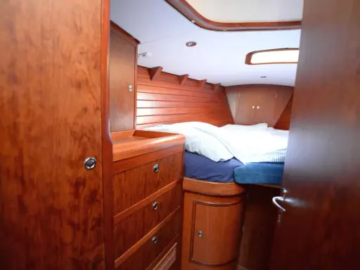 Gemütliches Bett mit gestreifter Bettwäsche im Innenbereich einer Segelyacht. Holzverkleidung und Schränke schaffen eine warme Atmosphäre.