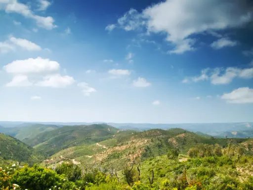 Grüne Hügel und Täler in Monchique, Portugal, unter einem weiten Himmel mit weißen Wolken.