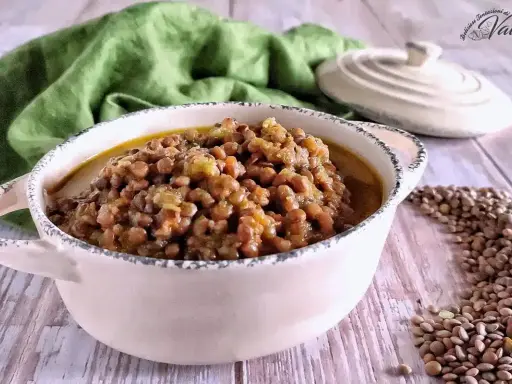 Un invitante piatto di lenticchie in umido, servito in una ciotola rustica, con un panno verde sullo sfondo.