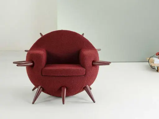 A round, burgundy armchair with pointed legs and armrests, in a minimalist room.