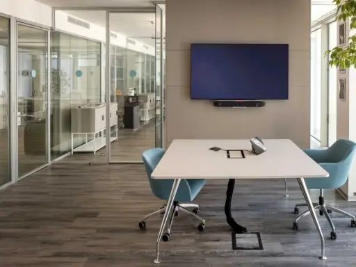 Un bureau futuriste avec une table de réunion, des chaises bleues, un écran mural et des cloisons vitrées.