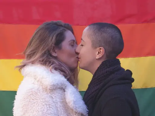 Deux femmes s'embrassent tendrement devant un drapeau arc-en-ciel, une belle représentation de l'amour saphique.