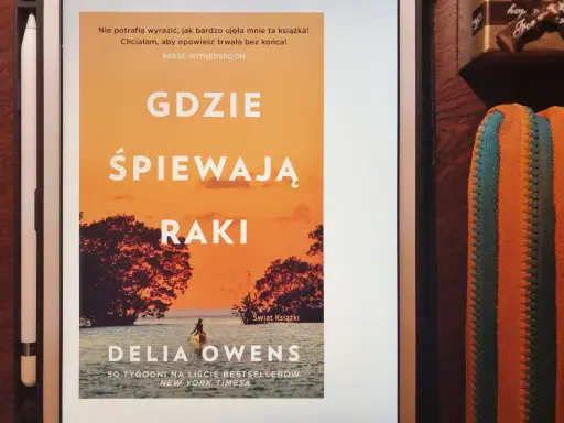 Dziewczyna z bagien na okładce książki "Gdzie śpiewają raki". Samotna postać w kajaku na tle zachodzącego słońca.