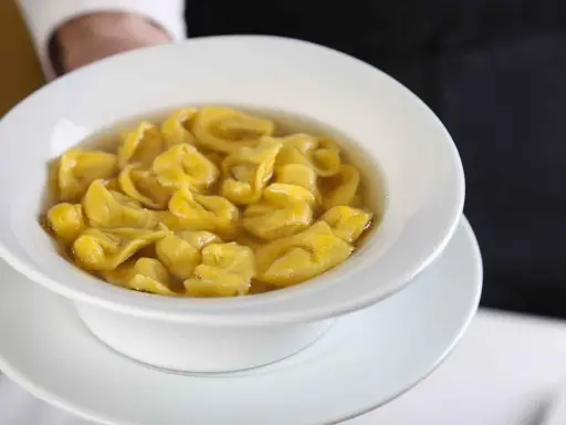 Un piatto fumante di tortellini in brodo, un classico comfort food italiano, servito in una ciotola bianca.