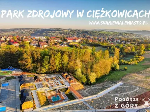 Widok z lotu ptaka na park zdrojowy w Ciężkowicach z placem zabaw, basenem i drewnianymi altanami.