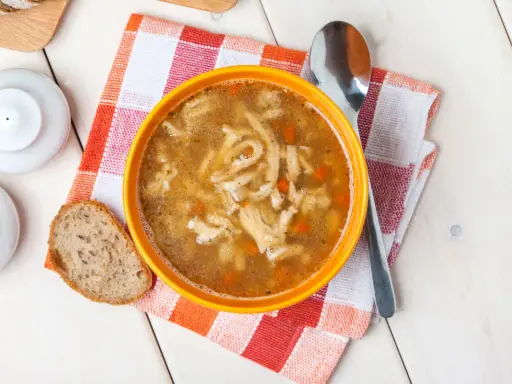 Aromaticzne flaki po zamojsku w pomarańczowej misce, obok kromka chleba i łyżka. Pyszne danie gotowe do spożycia.
