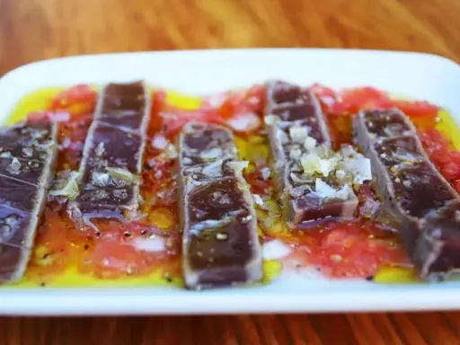 Tiras de atún marinado sobre rodajas de tomate y cítricos, un delicioso plato de comida típica de Huelva.