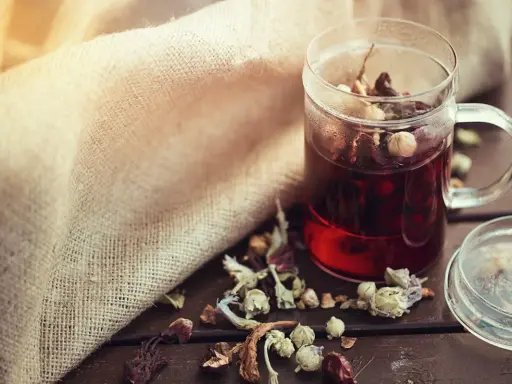 Infusion rouge dans une tasse en verre, entourée d'herbes séchées. Un remède naturel diurétique à portée de main.