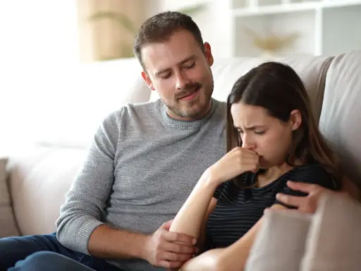 Un homme réconforte une femme en pleurs, son regard suggère une manipulation subtile, un exemple de pervers narcissique.