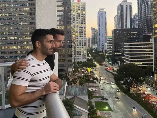 Two men embrace on a balcony overlooking a city street, a scene reminiscent of some of the most gay cities in the US.
