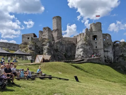 Ruiny zamku na skale, część wyżyny krakowsko-częstochowskiej, z widownią siedzącą na trawie.