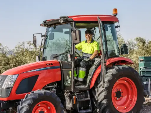 Un homme souriant conduit un tracteur rouge, une machine pour arracher des bambous, prêt à travailler dans un champ.