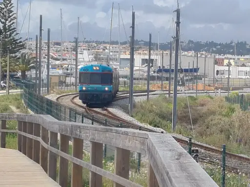 Ein Zug fährt auf den Gleisen in Richtung einer Marina mit vielen Segelbooten. Die Fahrt von Lissabon in die Algarve ist ein Erlebnis.