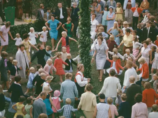 Många barn och vuxna dansar ringdans runt en midsommarstång i Sverige.