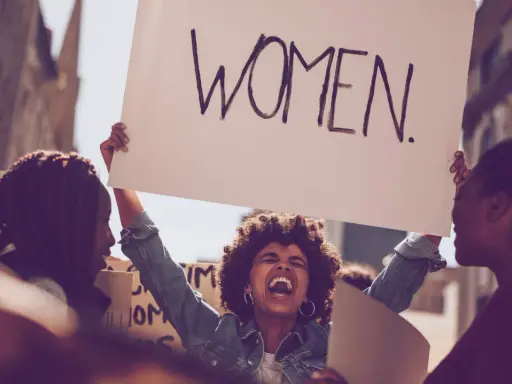 Frauen demonstrieren für Gleichberechtigung. Eine Frau hält ein Schild mit der Aufschrift "WOMEN". Das zeigt, was feminist ist: eine Stimme für Frauen.