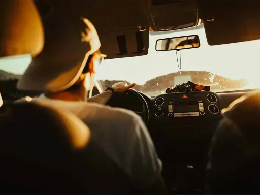 Hombre con gorra al volante, listo para planificar viaje en coche. El sol ilumina el interior del vehículo.