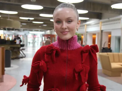 Zara Larsson i USA, klädd i en röd tröja med rosetter, ler mot kameran.
