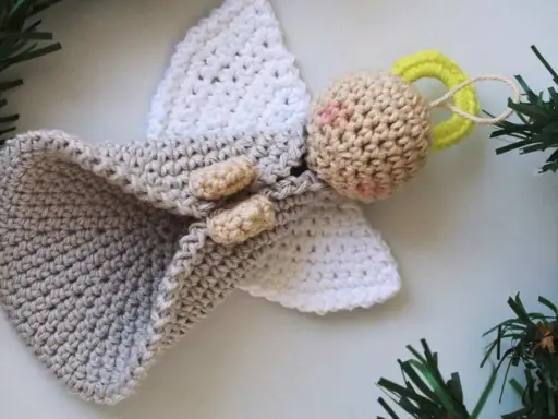 Un tierno angel amigurumi de ganchillo, con alas blancas y un cuerpo gris, adornado con ramitas verdes.