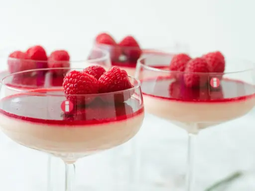 Flera glas med krämig pannacotta, toppad med hallon och en röd sås. En perfekt dessert i glas.