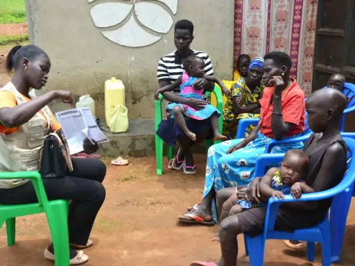 Kvinnor och barn samlas för vaccination i Uganda. En kvinna i väst visar upp papper.