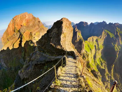 Pfad über Felsen zum Pico Ruivo, Madeira. Steile Hänge, grüne Vegetation und ein schmaler Weg mit Seilsicherung.