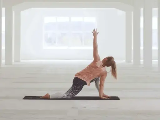 Kvinna utför en vriden yogaställning i ett ljust, öppet rum. Hon fokuserar på sin power yoga-träning.