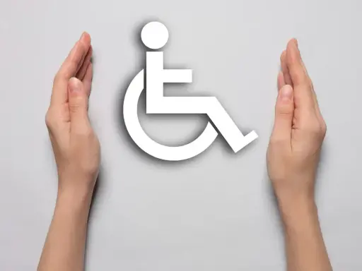 Dwie dłonie otaczają biały symbol osoby na wózku inwalidzkim, symbolizując wsparcie i akceptację dla osób z niepełnosprawnościami.
